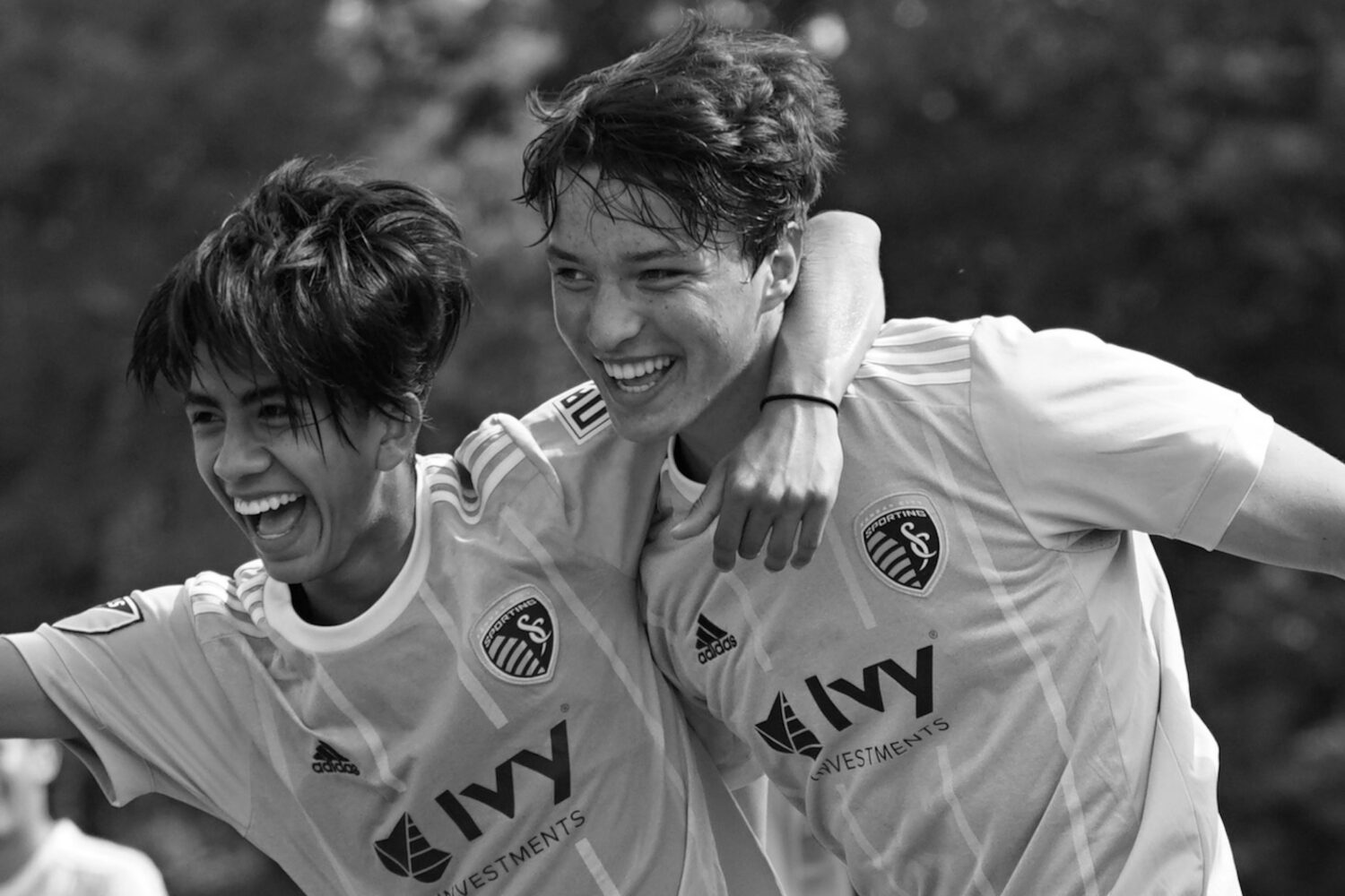 Two boys in soccer jerseys smiling with arms around each other.