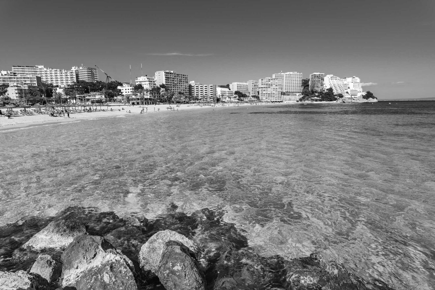 Coastal cityscape with clear water and rocks in foreground under a clear sky.