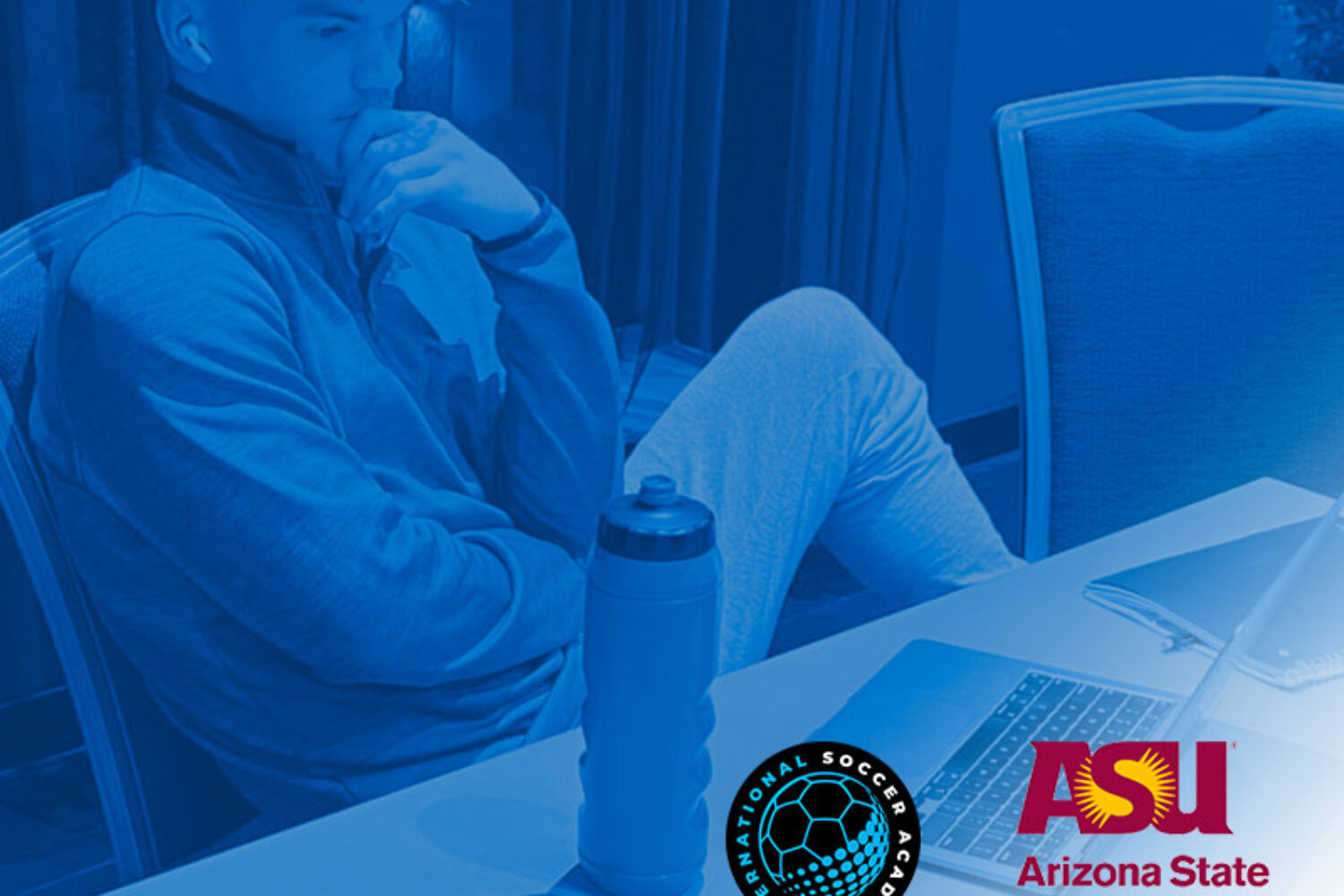 A person sits thoughtfully at a table with a laptop and water bottle, in a blue-tinted image.