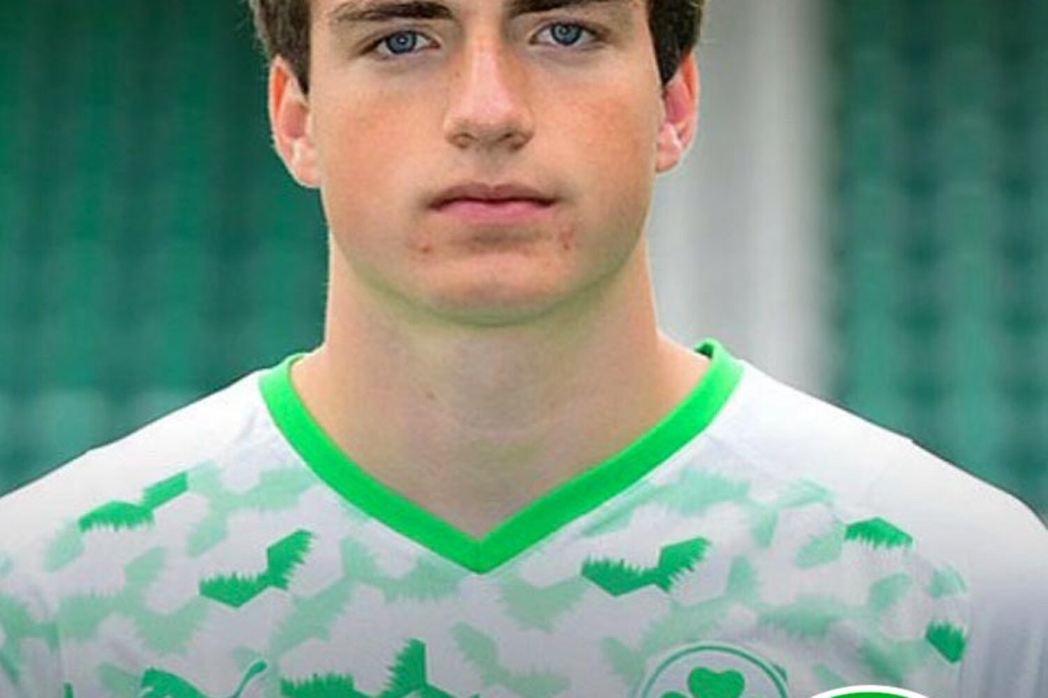 Close-up of a young man in a white and green sports jersey with a shamrock logo.