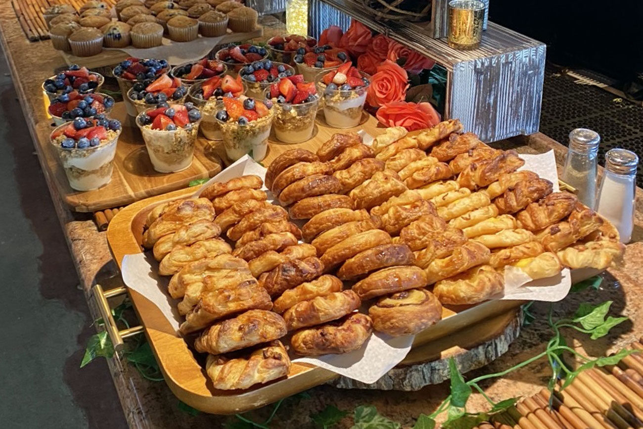 Assorted pastries and fruit parfaits displayed on a wooden table.