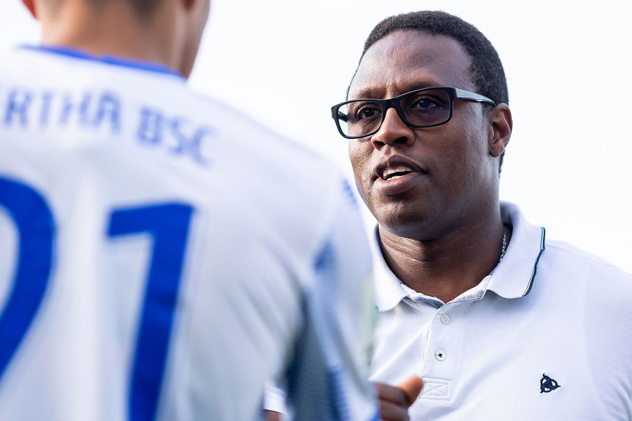 Man in glasses talking to a person in a sports jersey.