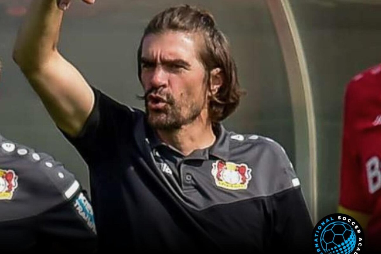 A man passionately gestures during a soccer event, wearing a Bayer Leverkusen shirt.
