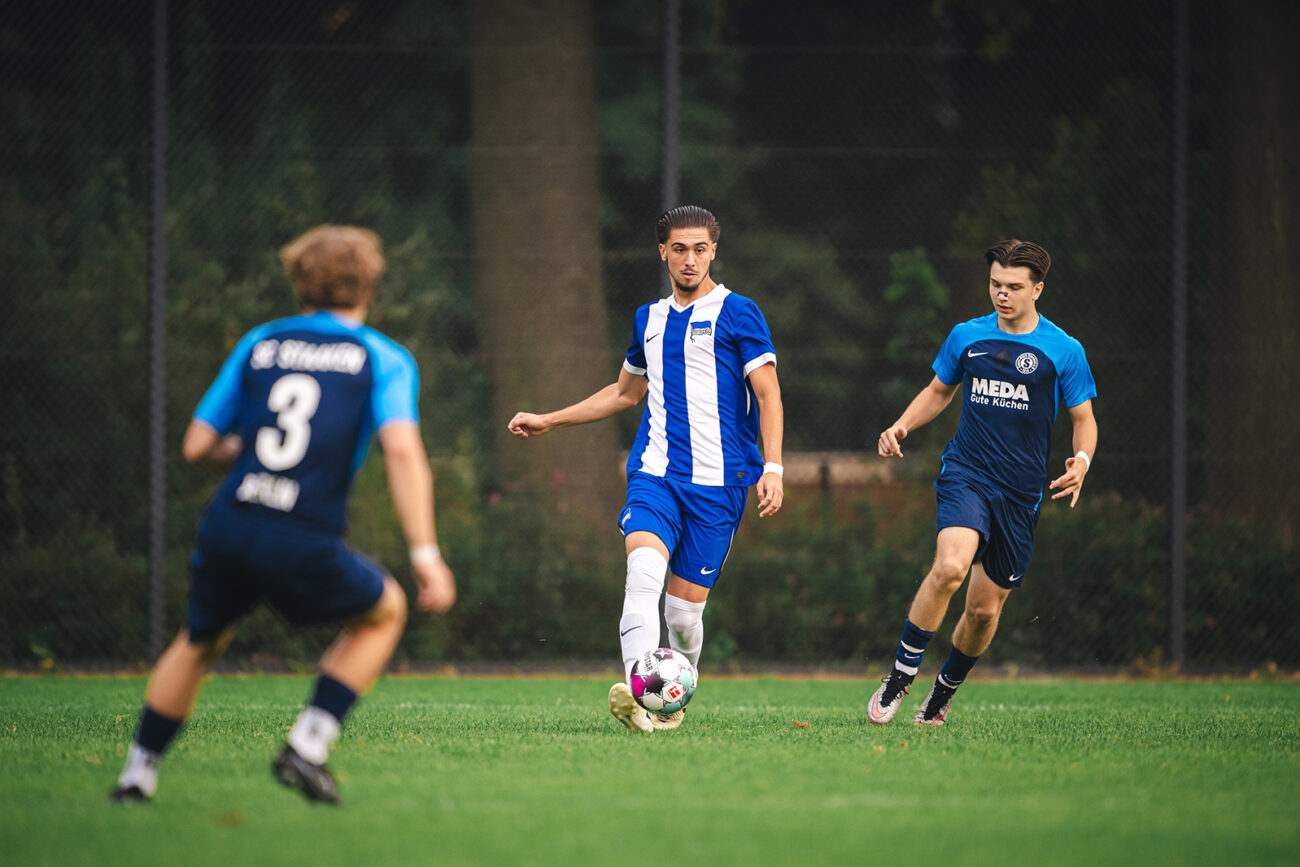 Soccer player in blue and white controls the ball while two opponents approach.