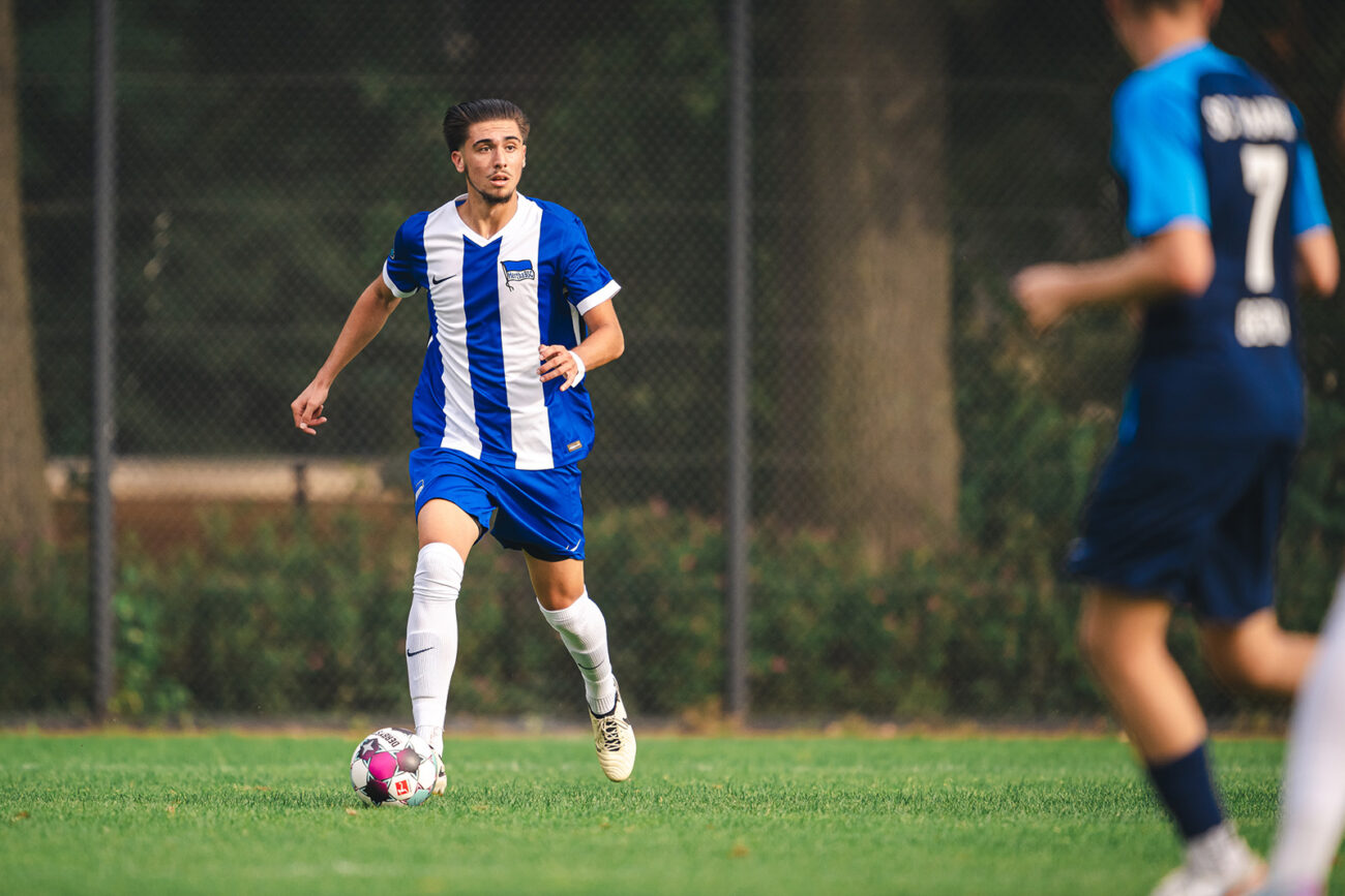 Young soccer player in blue and white dribbling the ball on a grassy field.