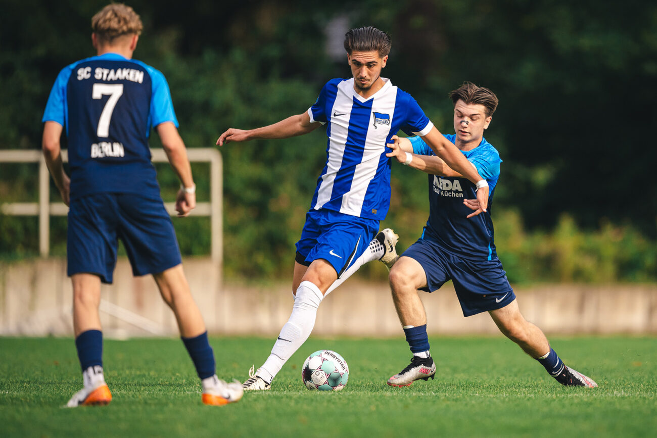 Soccer players from opposing teams compete intensely for the ball on a grassy field.