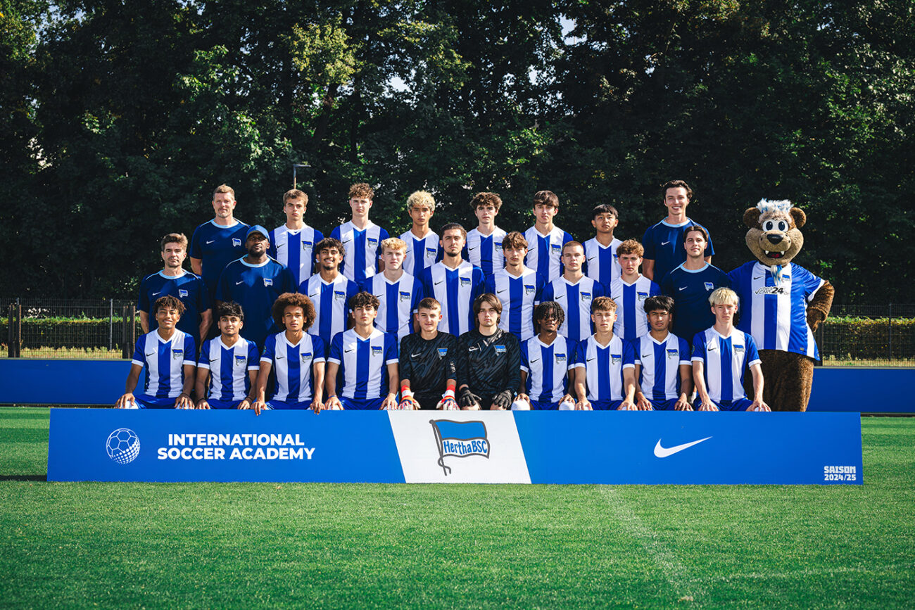 Youth soccer team in blue and white striped jerseys posing with coaches and mascot.
