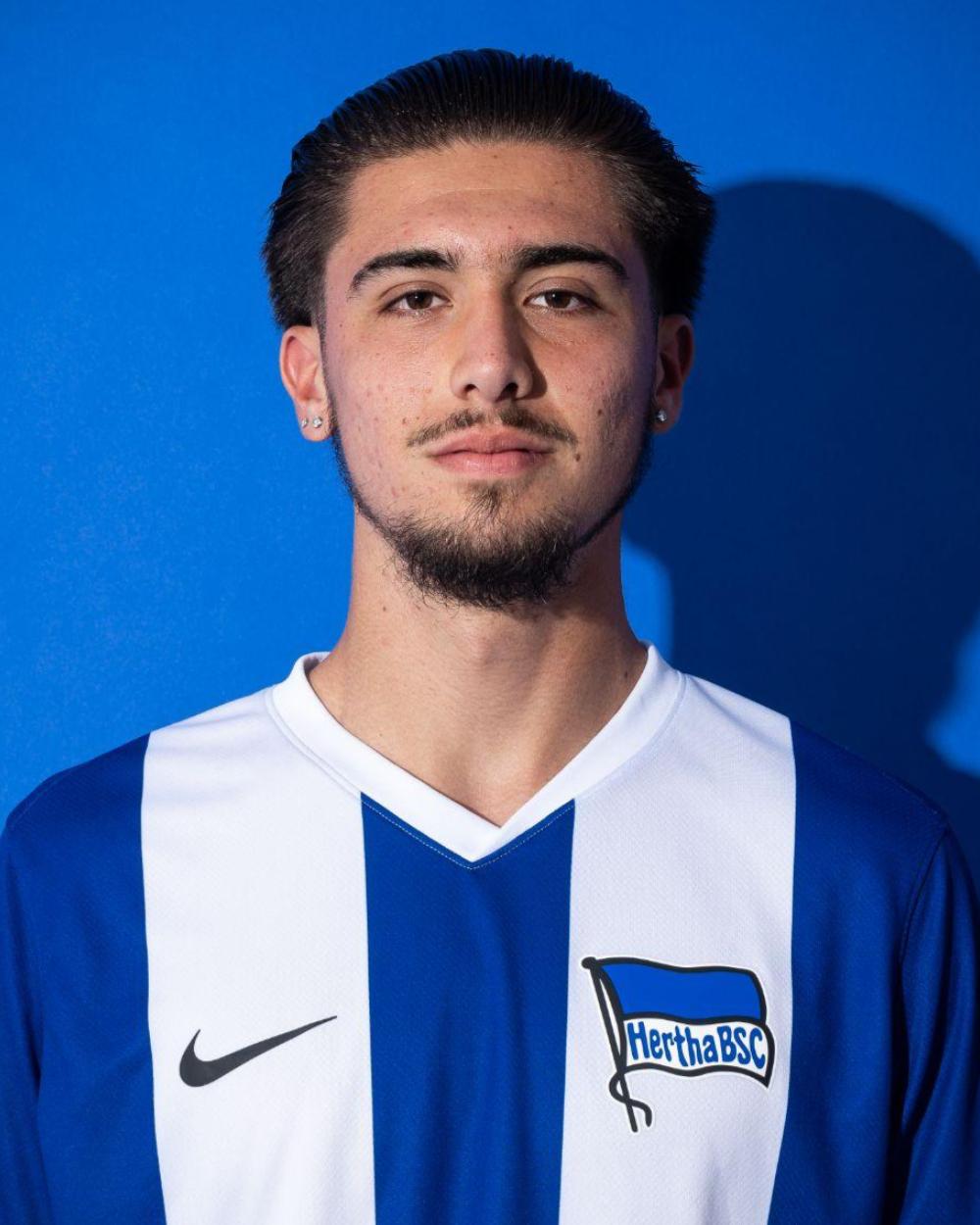 Portrait of a young man in a blue and white sports jersey against a blue background.