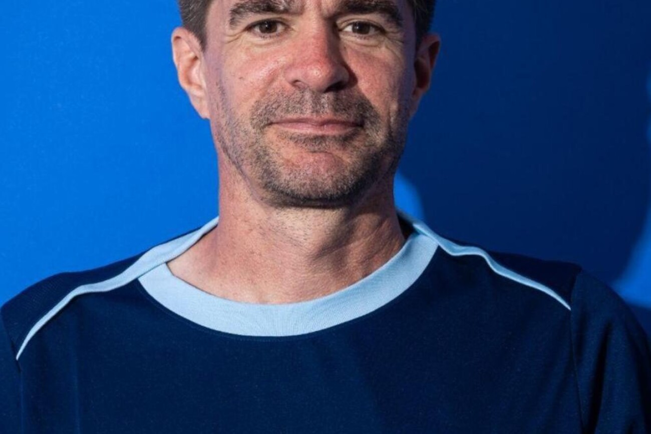 Man in a navy blue shirt smiling against a blue background.