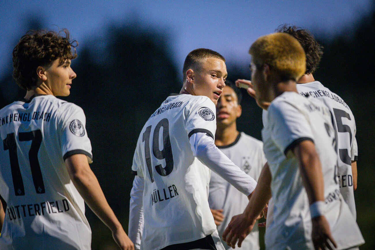 Young soccer players in white jerseys celebrating during a game at dusk.