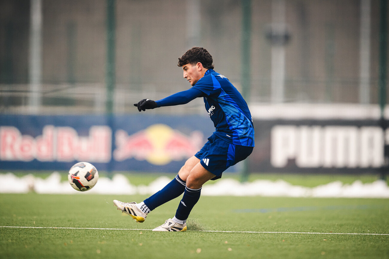 Soccer player in blue kit kicking a ball on the field.