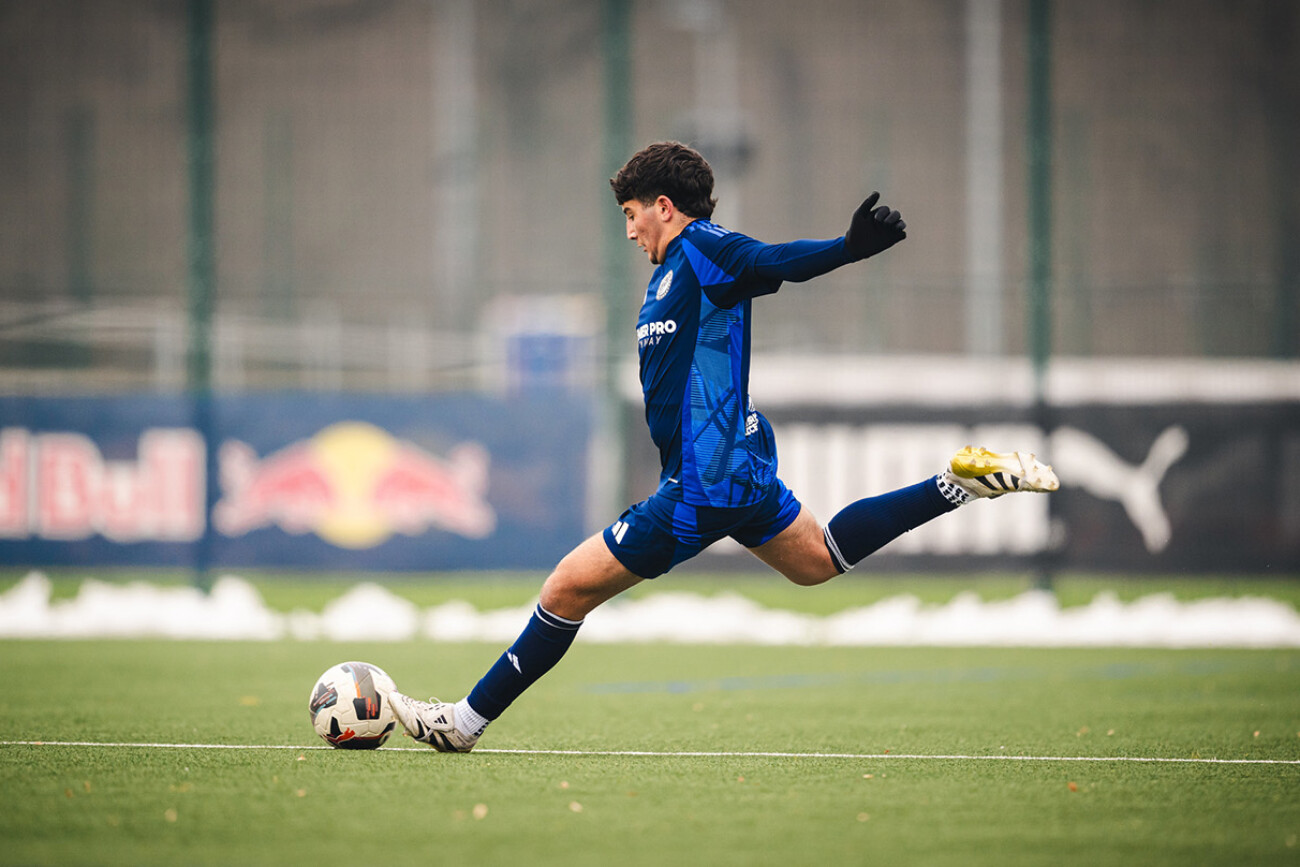 Soccer player in blue uniform kicking the ball on a green field.