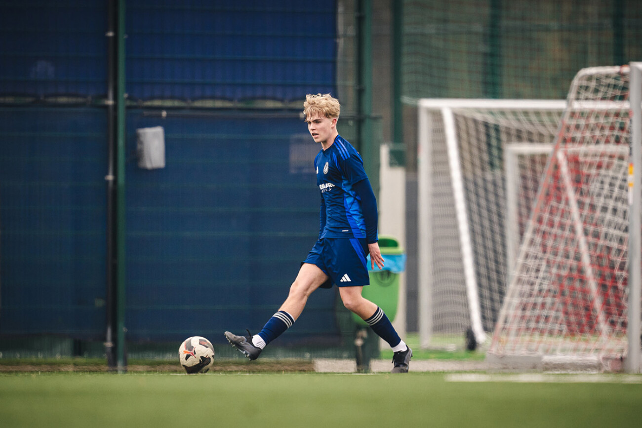 Young soccer player in blue uniform about to kick a ball on a field.