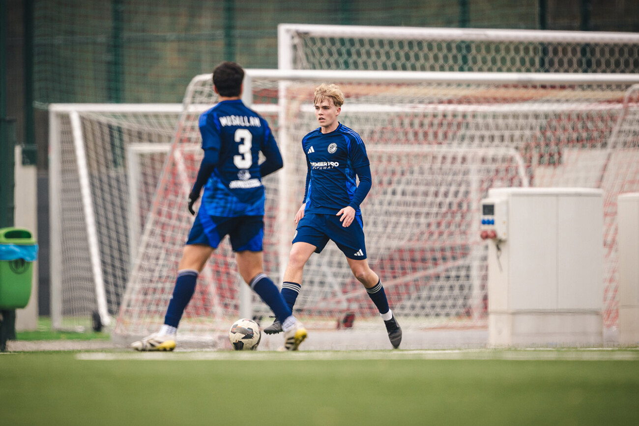 Two young soccer players in blue uniforms on the field near the goal.