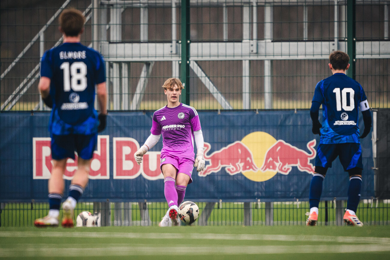 A soccer player in purple prepares to kick the ball between two opponents in blue.