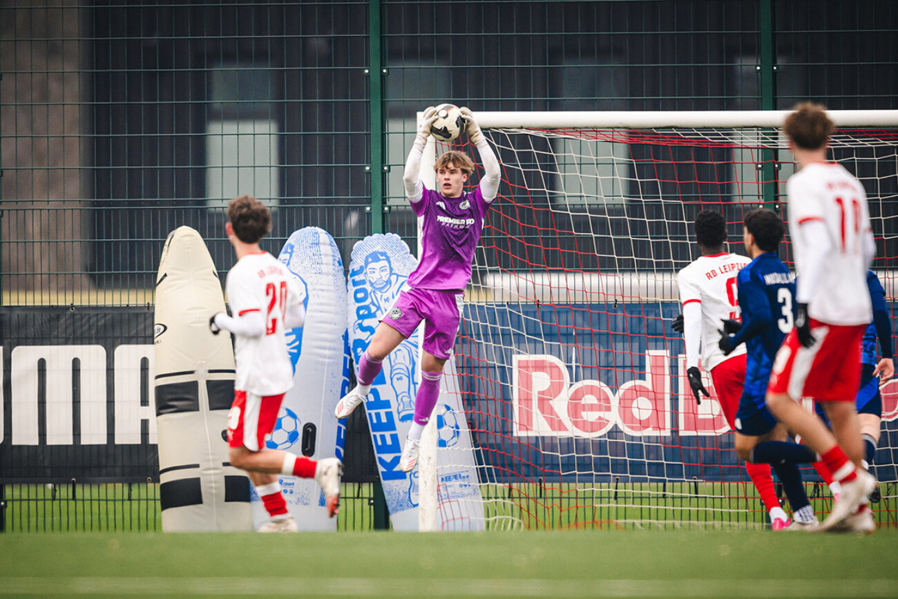 Youth soccer goalkeeper in purple jersey catching the ball mid-air.