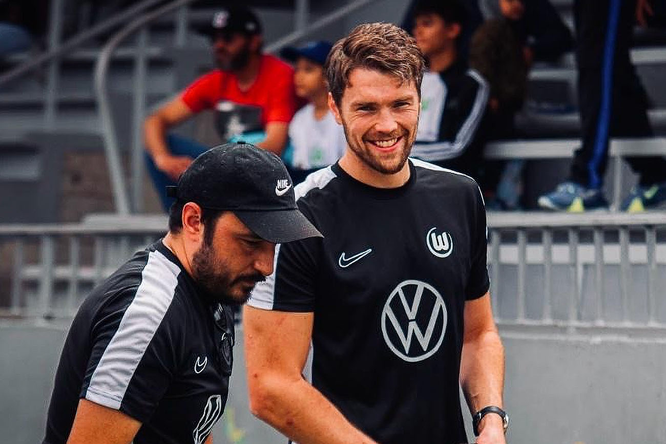 Two men in black Wolfsburg football training shirts, one smiling.