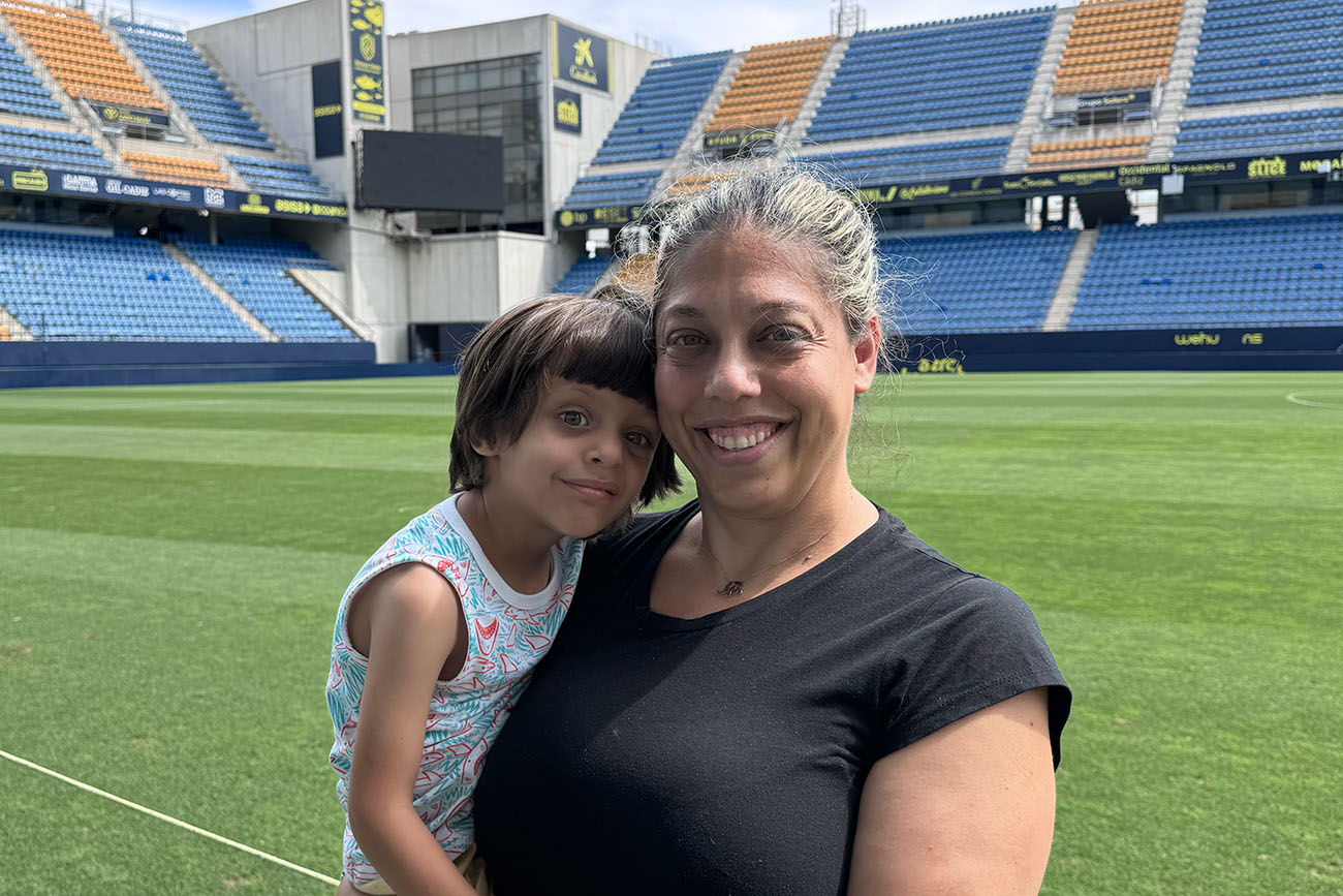 A smiling woman holding a child on a soccer field in a large stadium.
